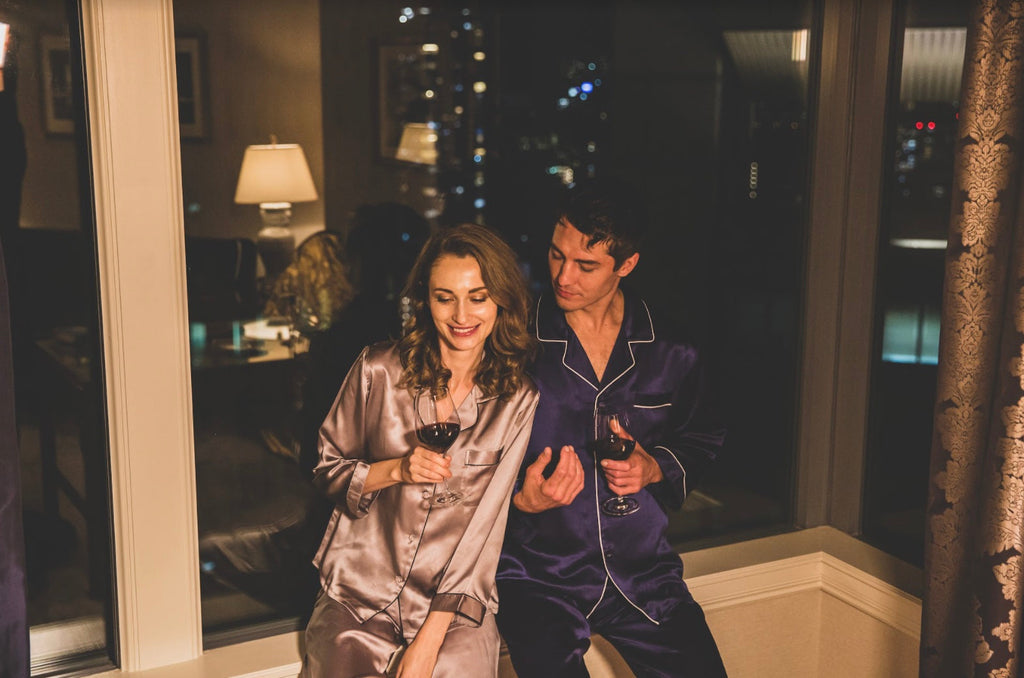 ホテルの窓際でシルクパジャマを着て、談笑するカップル